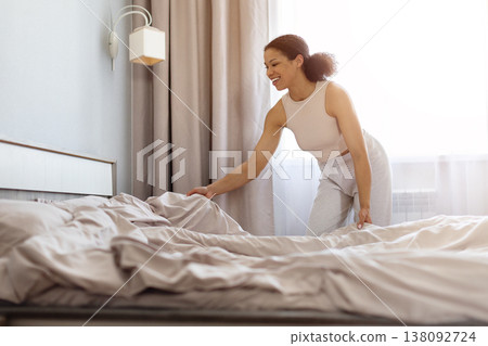 Smiling black woman making bed in morning, arranging blanket and pillows Smiling black woman making bed in morning, arranging blanket and pillows 138092724