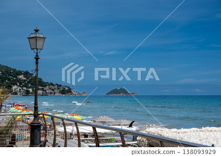 Alassio beach in the ligurian riviera, showing colorful umbrellas, the tranquil sea, a classic street lamp, and gallinara island under a clear blue sky Alassio beach in the ligurian riviera, showing colorful umbrellas, the tranquil sea, a classic street lamp, and gallinara island under a clear blue sky 138093929