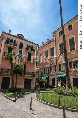 Italian buildings standing around a charming town square in alassio, liguria, featuring traditional architecture, lush palm trees, and clear blue sky on a sunny day Italian buildings standing around a charming town square in alassio, liguria, featuring traditional architecture, lush palm trees, and clear blue sky on a sunny day 138093932