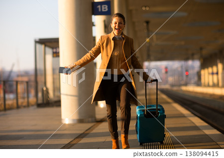Joyful Woman with Blue Suitcase Walking at Train Station Joyful Woman with Blue Suitcase Walking at Train Station 138094415