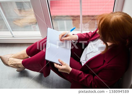 Woman with fiery hair revises document while sipping coffee Woman with fiery hair revises document while sipping coffee 138094589
