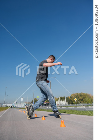 A Caucasian man rollerblades around the slalom course. A Caucasian man rollerblades around the slalom course. 138095234