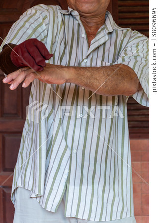 Senior man wearing glove on prosthetic arm highlighting disability support rehabilitation independence and daily self care routine in home environment with copy space 138096695