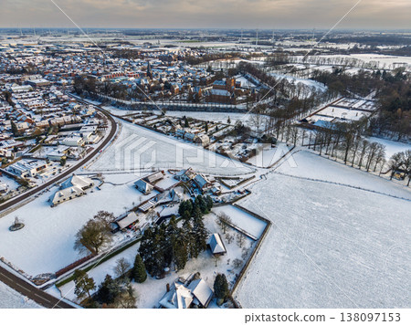 Panoramic aerial view of a snowy European town featuring Huis Bergh castle. A scenic winter landscape with frosted fields, residential houses, and wind turbines stretching to the horizon. Panoramic aerial view of a snowy European town featuring Huis Bergh castle. A scenic winter landscape with frosted fields, residential houses, and wind turbines stretching to the horizon. 138097153