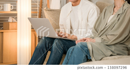 A young Asian couple sitting on the sofa in the living room and looking at a laptop A young Asian couple sitting on the sofa in the living room and looking at a laptop 138097296