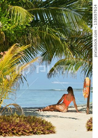 A beautiful tanned girl with an athletic physique in a swimsuit looks at the sea through palm trees on the personal beach of the villa on a sunny day in the Maldives, she is happy and posing A beautiful tanned girl with an athletic physique in a swimsuit looks at the sea through palm trees on the personal beach of the villa on a sunny day in the Maldives, she is happy and posing 138097614