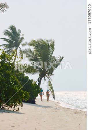 A beautiful tanned girl in a swimsuit and men walking along the white beach at sunset in the Maldives, they are happy, posing for a photographer A beautiful tanned girl in a swimsuit and men walking along the white beach at sunset in the Maldives, they are happy, posing for a photographer 138097690