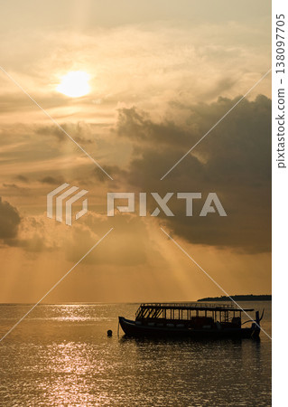 Magical sunset with orange sky at dusk on Maldives islands, silhouette of a tourist boat, the rays of the sun through the clouds, reflection on the water in beach, no people  138097705