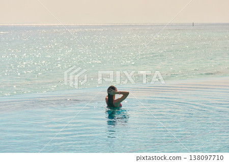 A beautiful tanned girl with an athletic physique in a swimsuit is at the edge of the pool of the villa pool on a sunset in the Maldives, she is happy and posing A beautiful tanned girl with an athletic physique in a swimsuit is at the edge of the pool of the villa pool on a sunset in the Maldives, she is happy and posing 138097710