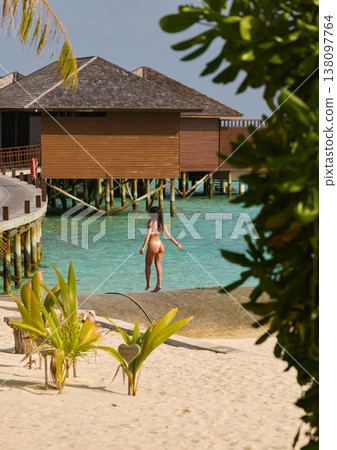 A beautiful tanned girl is wearing a swimsuit with an athletic physique stands on the beach of the villa on a sunny day in the Maldives, she is happy and posing A beautiful tanned girl is wearing a swimsuit with an athletic physique stands on the beach of the villa on a sunny day in the Maldives, she is happy and posing 138097764