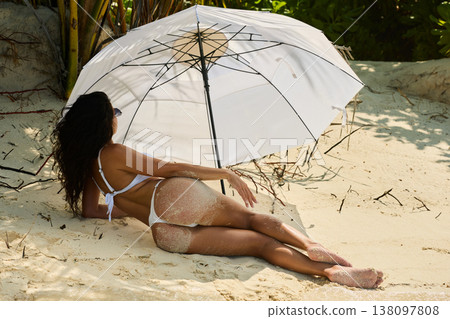 A beautiful tanned girl with an athletic physique in a swimsuit is posing on the personal beach of the villa on a sunny day in the Maldives, she is lying under an umbrella, she is happy and posing 138097808