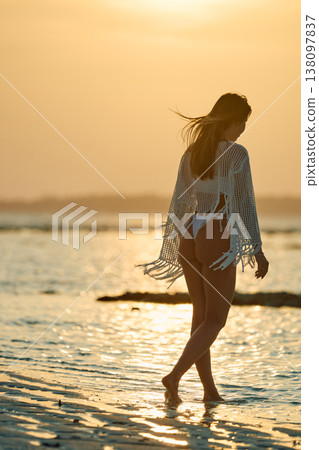 A beautiful tanned girl in a swimsuit stands along a white beach at sunset in the Maldives, she is happy, posing for a photographer 138097837