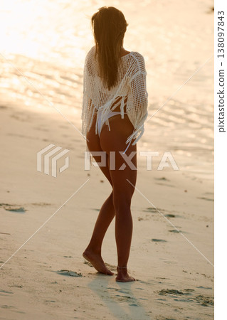 A beautiful tanned girl in a swimsuit stands along a white beach at sunset in the Maldives, she is happy, posing for a photographer 138097843