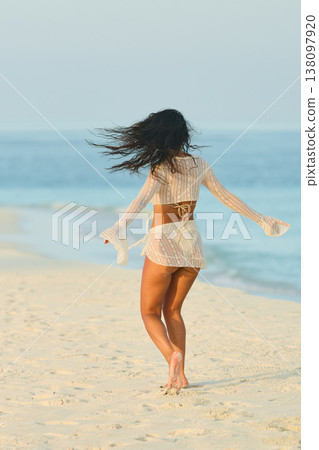 A beautiful tanned girl in a swimsuit runs along a white beach at sunset in the Maldives, she is happy, posing for a photographer 138097920