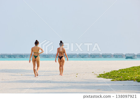 A beautiful tanned girls in a swimsuit walking along the white beach at sunset in the Maldives, they are happy, posing for a photographer 138097921