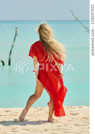 A beautiful tanned girl is wearing in red cape fun on the personal beach of the villa on a sunny day in the Maldives, she is happy and posing A beautiful tanned girl is wearing in red cape fun on the personal beach of the villa on a sunny day in the Maldives, she is happy and posing 138097925