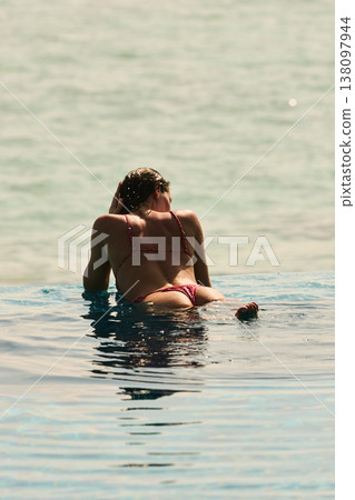 A beautiful tanned girl with an athletic physique in a swimsuit is at the edge of the pool of the villa pool on a sunset in the Maldives, she is happy and posing A beautiful tanned girl with an athletic physique in a swimsuit is at the edge of the pool of the villa pool on a sunset in the Maldives, she is happy and posing 138097944