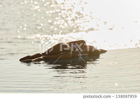 A beautiful tanned girl with an athletic physique in a swimsuit is at the edge of the pool of the villa pool on a sunset in the Maldives, she is happy and posing A beautiful tanned girl with an athletic physique in a swimsuit is at the edge of the pool of the villa pool on a sunset in the Maldives, she is happy and posing 138097959