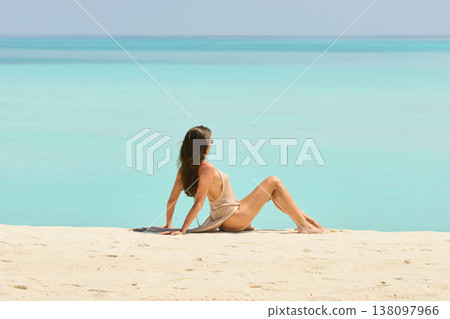 A beautiful tanned girl with an athletic physique in a swimsuit is siting on the beach on a sunny day in the Maldives, she is happy and posing 138097966