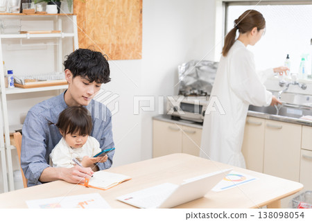 A young father working on the phone while taking care of his child in the dining room: A scene of childcare while working from home. 138098054