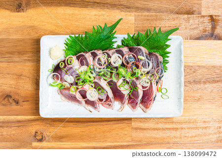 Japanese sashimi dish with condiments, featuring seared bonito, served on a wooden table. Japanese sashimi dish with condiments, featuring seared bonito, served on a wooden table. 138099472
