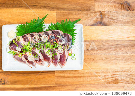 Japanese sashimi dish with condiments, featuring seared bonito, served on a wooden table. Japanese sashimi dish with condiments, featuring seared bonito, served on a wooden table. 138099473