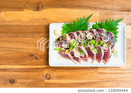 Japanese sashimi dish with condiments, featuring seared bonito, served on a wooden table. Japanese sashimi dish with condiments, featuring seared bonito, served on a wooden table. 138099484