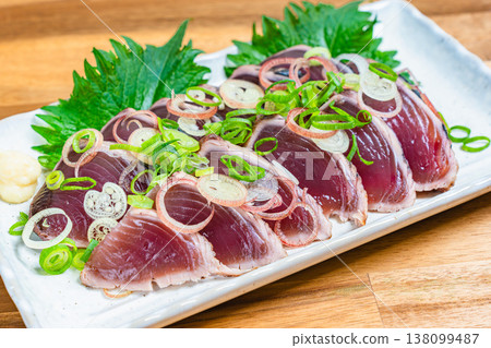 Japanese sashimi dish with condiments, featuring seared bonito, served on a wooden table. Japanese sashimi dish with condiments, featuring seared bonito, served on a wooden table. 138099487