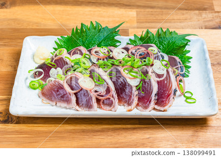 Japanese sashimi dish with condiments, featuring seared bonito, served on a wooden table. Japanese sashimi dish with condiments, featuring seared bonito, served on a wooden table. 138099491