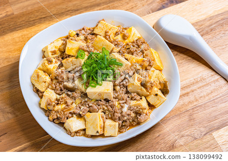 麻婆豆腐,用白色盤子盛裝的中國菜,在木桌上烹調的家常菜。 麻婆豆腐,用白色盤子盛裝的中國菜,在木桌上烹調的家常菜。 138099492