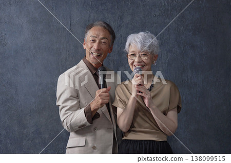 Senior men and women singing karaoke, black background, portrait, looking at camera Senior men and women singing karaoke, black background, portrait, looking at camera 138099515