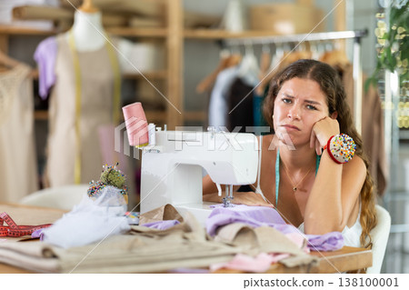 Sad dressmaker sitting at sewing machine in studio Sad dressmaker sitting at sewing machine in studio 138100001
