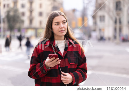 Girl traveler walks through tourist area of European city with phone Girl traveler walks through tourist area of European city with phone 138100034
