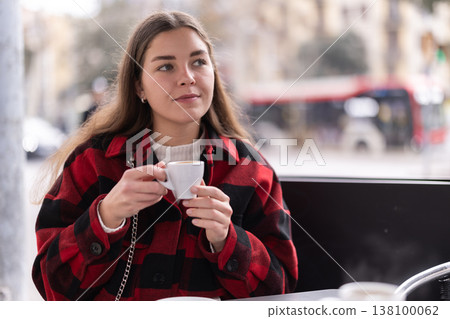 Girl in plaid jacket sits at table in street cafe, drink tea 138100062