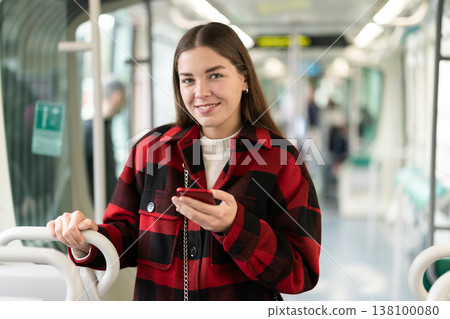 Girl with long hair standing in tram with phone Girl with long hair standing in tram with phone 138100080