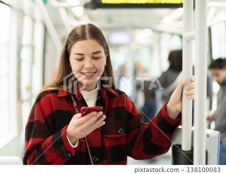 Girl is standing with phone in tram car, getting to work Girl is standing with phone in tram car, getting to work 138100083