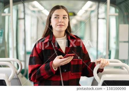 Girl with long hair standing in tram with phone Girl with long hair standing in tram with phone 138100090