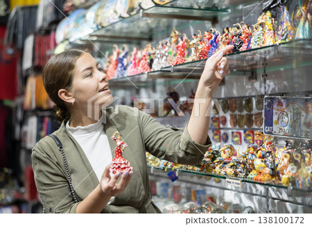 Cheerful female tourist choosing gift decorative dancer figurines at tourist shop Cheerful female tourist choosing gift decorative dancer figurines at tourist shop 138100172