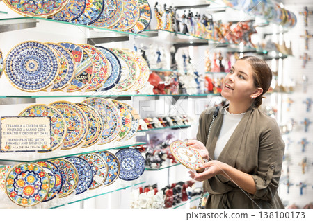 Young woman looks at decorative saucer at souvenir market Young woman looks at decorative saucer at souvenir market 138100173