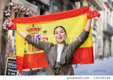 Happy young woman waving the flag of Spain on city street 138100188