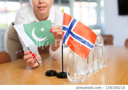 Unrecognizable girl sets midget flags of Norway and Pakistan before international negotiations 138100218