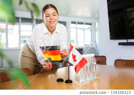 Positive young woman putting little flag of Germany on table next to the flag of Canada Positive young woman putting little flag of Germany on table next to the flag of Canada 138100223