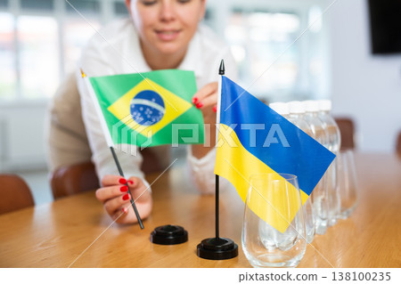 National table flags of Brazil and Ukraine in hands of woman preparing to negotiations National table flags of Brazil and Ukraine in hands of woman preparing to negotiations 138100235
