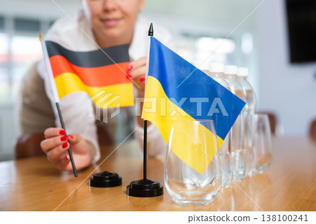 Woman setting national flags of Germany and Ukraine on negotiating table Woman setting national flags of Germany and Ukraine on negotiating table 138100241
