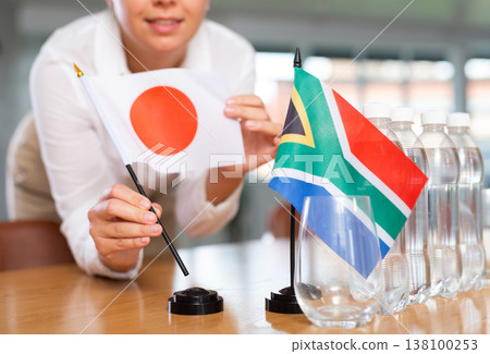 Little flag of South Africa on table and flag of Japan put next to it by young woman Little flag of South Africa on table and flag of Japan put next to it by young woman 138100253