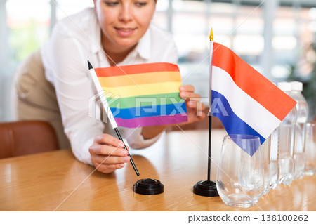 Preparing for business negotiations - woman sets small flags of countries of Netherlands and LGBT on table Preparing for business negotiations - woman sets small flags of countries of Netherlands and LGBT on table 138100262