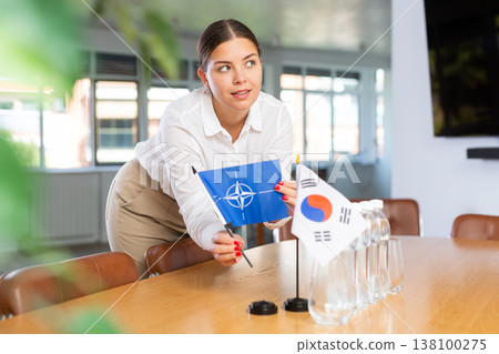 Preparing for business negotiations - woman sets small flags of countries of NATO (OTAN) and South Korea on table Preparing for business negotiations - woman sets small flags of countries of NATO (OTAN) and South Korea on table 138100275