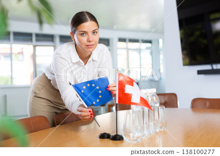 Positive young woman putting little flag of European Union on table next to the flag Positive young woman putting little flag of European Union on table next to the flag 138100277