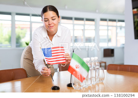 Positive young woman putting little flag of the USA on table next to the flag of Iran Positive young woman putting little flag of the USA on table next to the flag of Iran 138100294