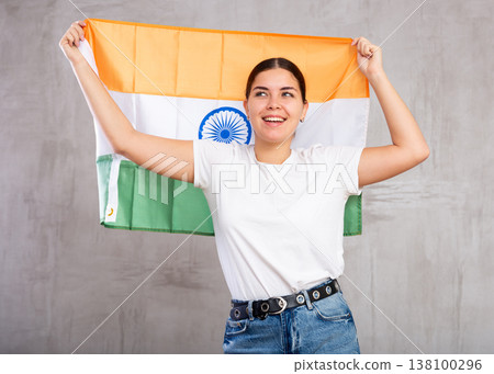 Joyful smiling young woman waving flag of India against gray wall background 138100296